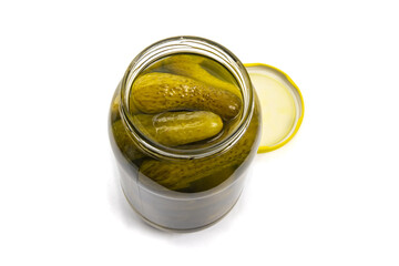An opened glass jar of grocery store baby dill pickles with the lid beside isolated on white