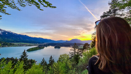 Happy woman enjoying the panoramic sunset view on Lake Faak from Taborhoehe in Carinthia, Austria, Europe. Austrian Alps. Water surface reflecting soft sunlight. Remote alpine landscape in summer