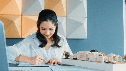 Portrait of young beautiful architect engineer measuring house model by using pencil while taking a...