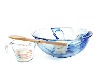 A blue glass mixing bowl with butter and a measuring cup of flour isolated on white