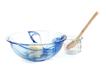 a blue glass mixing bowl with butter and an empty measuring cup isolated on white