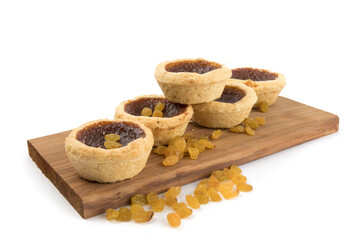 fresh baked butter tarts stacked on a wooden board with loose raisins isolated on white