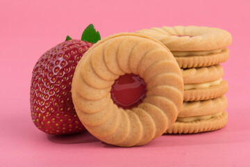 close up of strawberry fruit creme cookies and a large red strawberry isolated on pink