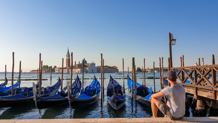 Tourist man on water edge watching gondolas moored by Saint Mark square in city Venice, Veneto,...