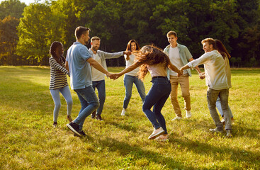 Fototapeta premium Group of cheerful and carefree best friends in park are circling together holding hands. Young people in casual clothes gathered together for weekend in park in summer and dance in circle.