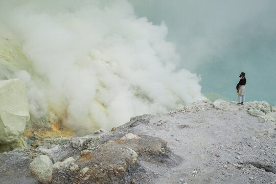 Traveller wearing respirator stands in volcano crater with sulfur gas