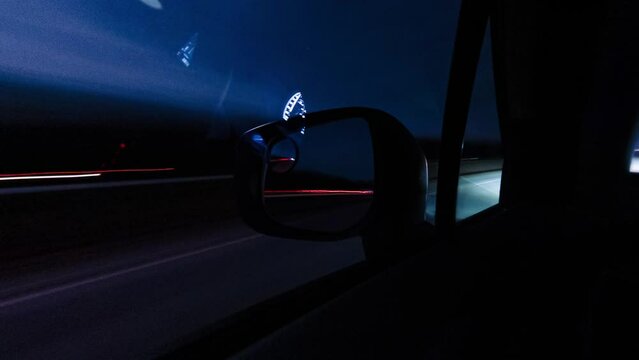 Car mirror and window reflection while driving at night timelapse. Long exposure time lapse from the car on highway. Driving at night city with bright lights and traffic. Fast moving hyperlapse.