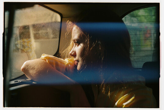 A redheaded girl in a yellow shirt traveling in the back seat of a car