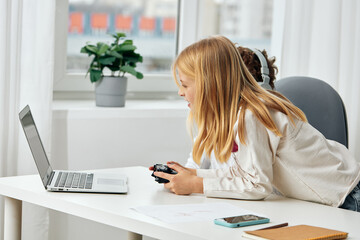 Happy Caucasian children studying online at home, sitting at a study table with laptops, tablets, and headphones The boy and girl are engaged in elearning, typing and playing educational games,