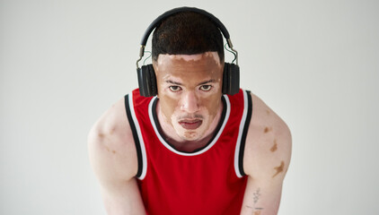 Man, portrait and fitness with headphones in studio for music listening, vitiligo and workout. Unique skin, basketball player and health by white background with headset for training body and audio