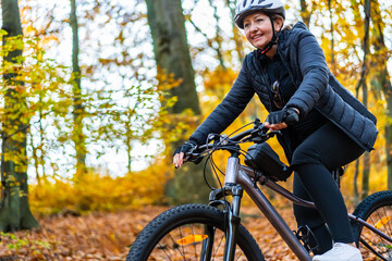 Woman riding bicycle in city forest in autumnal scenery
