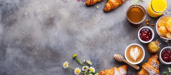 Fototapeta na wymiar Top-down view of a continental breakfast spread including coffee, orange juice, croissants, jam, honey, and flowers, set against a grey stone worktop. Ample space for text.