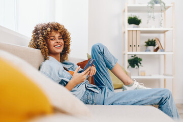 Happy Woman Relaxing on a Cozy Sofa, Holding Mobile Phone and Smiling