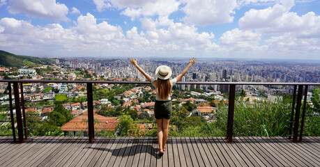Tourism in Belo Horizonte, Brazil. Panoramic banner view of tourist woman with raising arms from beautiful belvedere in Belo horizonte, Minas Gerais, Brazil. - obrazy, fototapety, plakaty