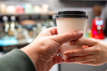 Close-up of a person’s hand holding a takeaway coffee cup in a cafe, with a blurred background