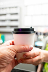 Close-up of a person’s hand holding a takeaway coffee cup in a cafe, with a blurred background