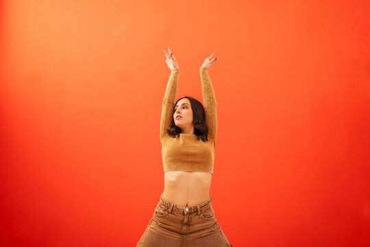 young generation z woman dancing in front of an orange background