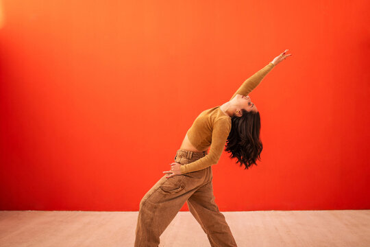 young generation z woman dancing in front of an orange background