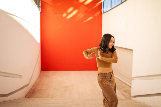 young generation z woman dancing in front of an orange background
