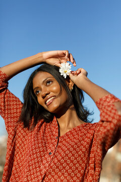 Smiling woman putting flowers on the hair over blue sky