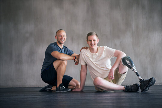 Physiotherapist, person with a disability and prosthetic leg and smile in physiotherapy, studio and gym. Male people, trainer and amputee for wellness, fitness and exercise in sports center - Powered by Adobe