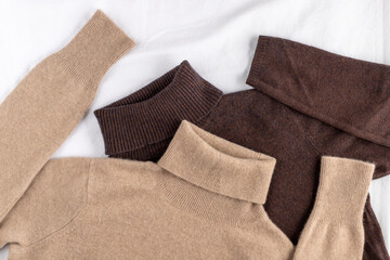 Soft sweaters of beige and of brown luxury natural cashmere lying on white linen background. ...