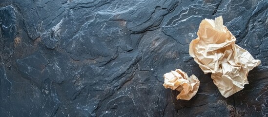 Crumpled paper sheet on a dark slate stone with space for text as a background for food. Overhead perspective. Idea.