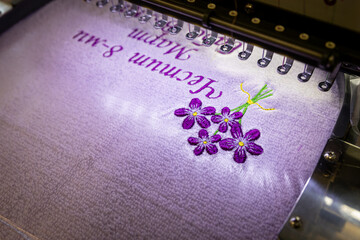 Machine embroidery of a bouquet of flowers on a purple cloth. Embroidery of a bouquet of purple flowers and an inscription. A gift for loved ones. Bulgarian holiday March 8. Women's Day.