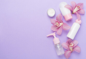 Bottles and jars with cream and orchids on color background, top view