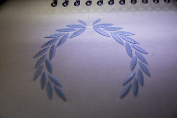 Embroidery design on white fabric with blue thread. Machine embroidery. Close up.