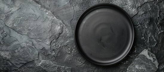 A black plate sits on a gray slate surface with no decorations, seen from above. There is empty space for adding text or other elements. - obrazy, fototapety, plakaty