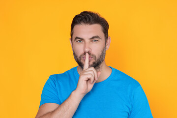 Shh man. Portrait of man showing shh taboo sign with finger to lips over yellow studio background....