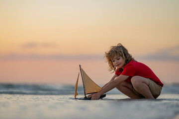 Kid play on the beach on a sunny day. Little sailor play with sailing boat in sea water. Child...