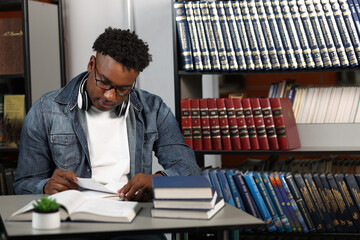 Young modern African-American professor prepares for classes in the office of the university. A dark-skinned man, a student in jeans, sitting at a table, flipping through a book