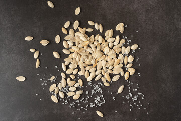 White pumpkin seeds on a dark background, close-up. Pumpkin seeds are scattered on the table along...