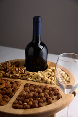 A bottle of wine and an empty glass glass on a stand made of wood with nuts on a gray background. Excellent serving of nuts and wine in a popular restaurant