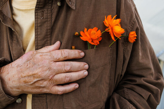 An elderly woman holds orange flowers tucked into her shirt pocket