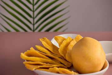 Selicious healthy snack candied mango beautifully laid out white plate, stands table against background of tropical green leaf. Slices sweet tropical mango fruit beautifully laid out on white platter