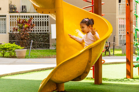 Una linda ni&ntilde;a de dos a&ntilde;os sonriente juega en un tobogan dentro del patio de un condominio.