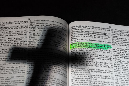 An open bible with a shadow of a cross and a highlighted verse. - Powered by Adobe