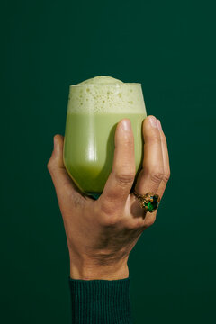 man holding a glass with iced matcha latte