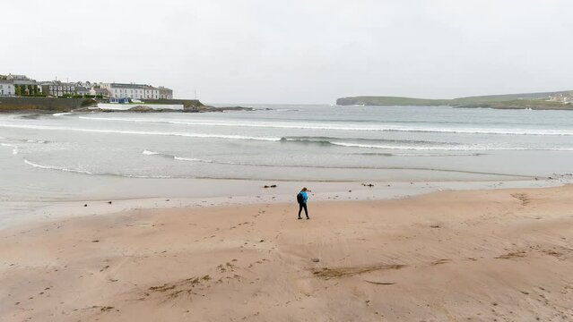 Young female tourist on the beach of Kilkee, small coastal town, popular as a seaside resort, located in horseshoe bay and protected from the Atlantic Ocean by the Duggerna Reef. Co. Clare, Ireland.