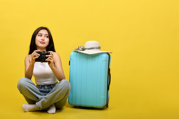 An advertisement for a large roomy travel suitcase by a girl sitting next to her with a camera. Young pretty brunette sitting cross-legged holding camera