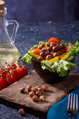 Delicious slicing of fresh vegetables and hazelnuts that stands in a plate on a wooden board. Tomato, pepper and nut salad drizzled with olive oil on a spectacular dark background.