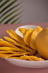 Close-up of slices of candied fruit, sweet, healthy yellow mango, neatly beautifully laid out on a white plate against a background of green tropical leaf. Neat serving of healthy delicious mango