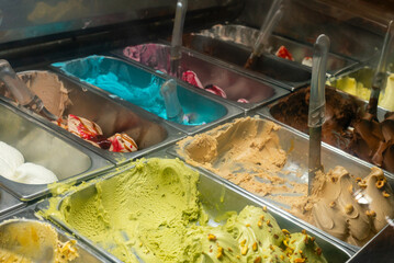 Tasty delicious ice cream and gelato with steel spoon above containers with assorted cold gelato in...