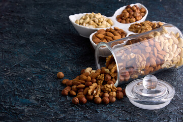 Assorted nuts in a dried fruit store on a gray textured background. On a gray table, nuts are laid out on a beautiful plate next to a scattered mixture from a glass jar. 