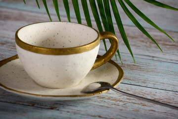 Beautiful antique tea pair, a saucer and a cup with a gold border stand on a wooden table. A silver teaspoon rests on a saucer of porcelain tea pair
