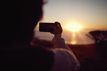 Hiking, photography and woman with phone at sunset, nature and mountain to relax on holiday adventure. Smartphone, trekking and person with view of orange sky, ocean and memory on vacation from back