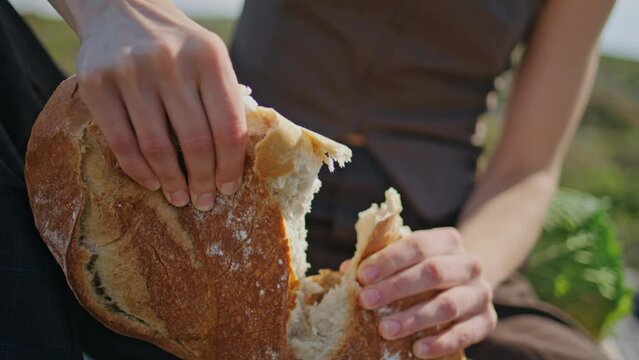 Hands breaking fresh bread on outdoor picnic closeup. Hungry girl baguette